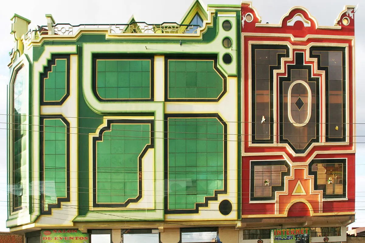 Zwei hohe Gebäude nebeneinander in El Alto, eines mit grün-cremefarbener Fassade aus kantigen Fenstern und eines in Rot mit gestuftem geometrischem Muster